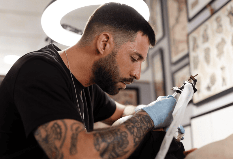 Close-up of a tattoo artist working on a detailed script tattoo.